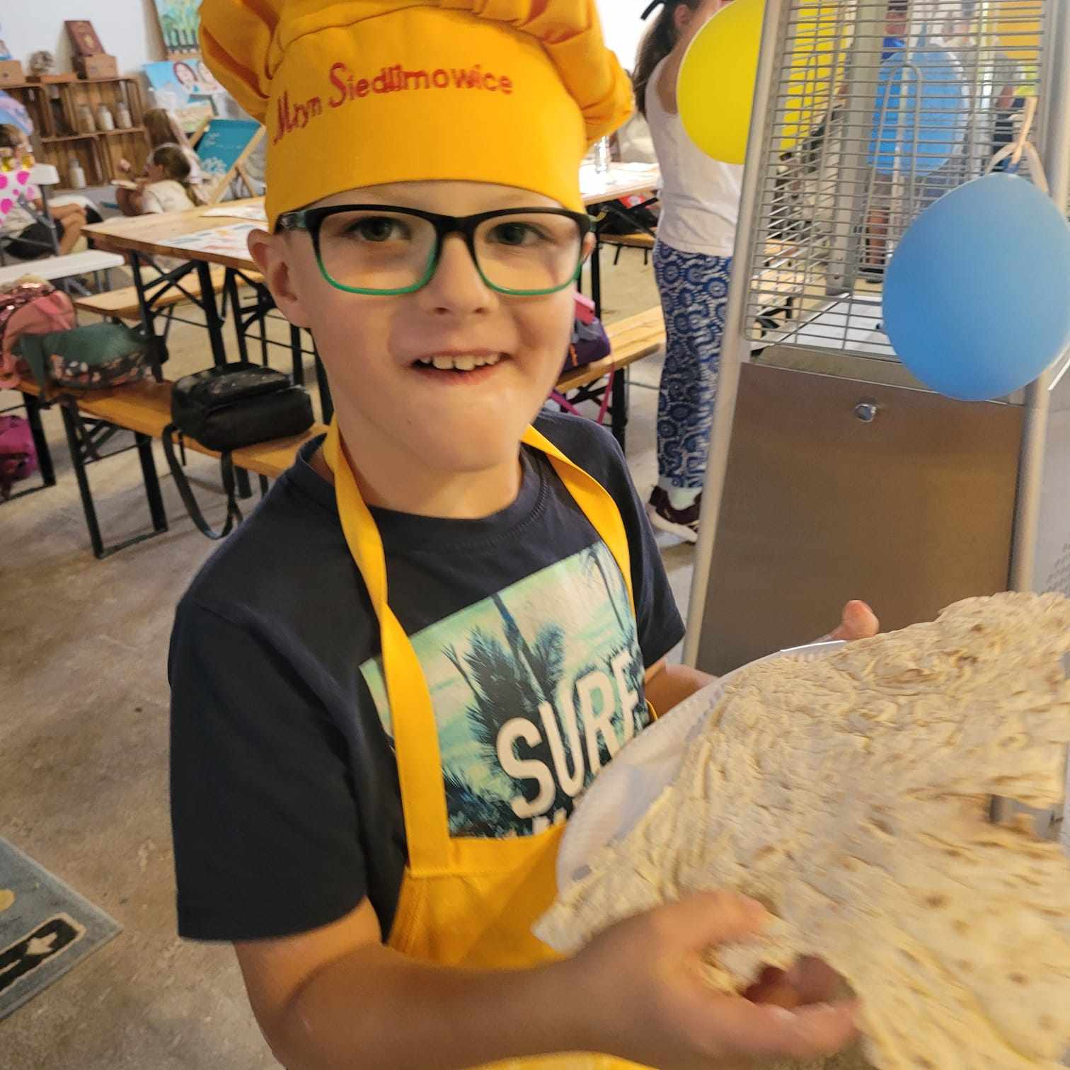 Chłopiec w czapce z napisem Młyn Siedlimowice trzymający w rękach ciasto