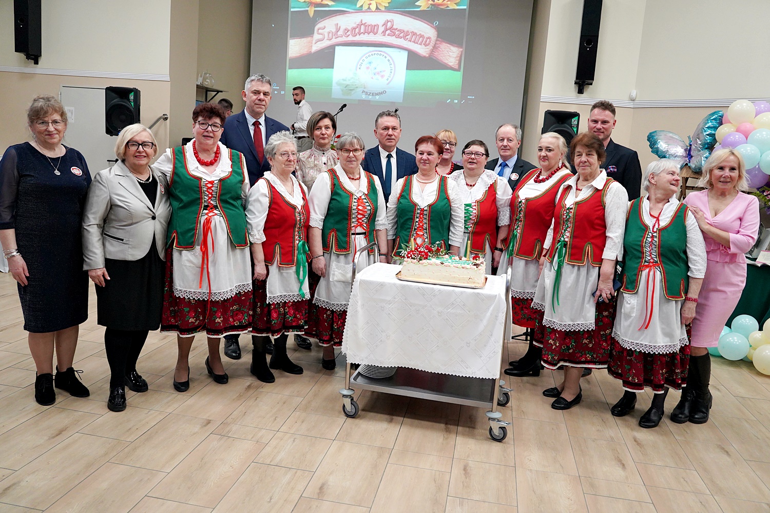 Gospodynie z Pszenna w otoczeniu gości stojące na świetlicy w Pszennie. W środku tort jubileuszowy.