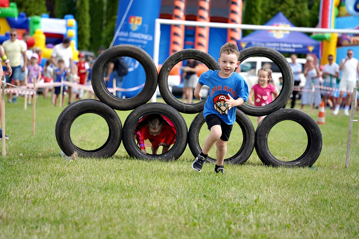 Biegnący chłopczyk po murawie boiwska, w tle opony