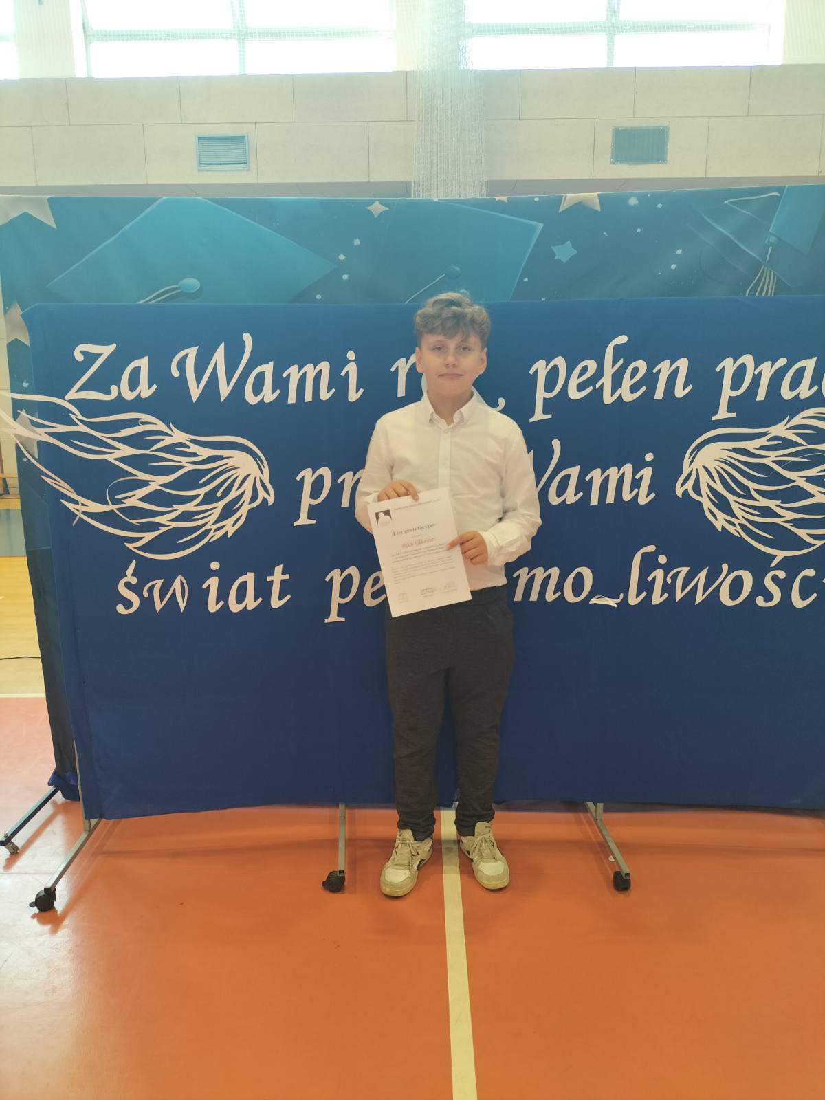 Uczeń Roch stojący z dyplomem na ściance