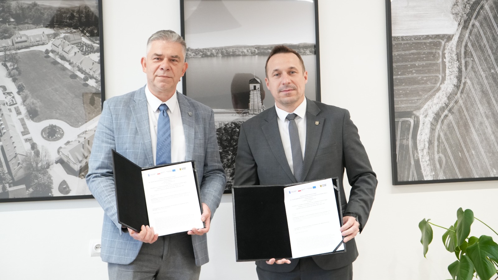 Wójt z marszałkiem trzymają umowy w eku, w tle obrazu biało-czarne